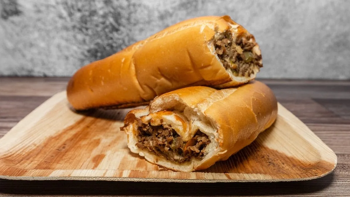 Two cheesesteak heroes on a wooden board